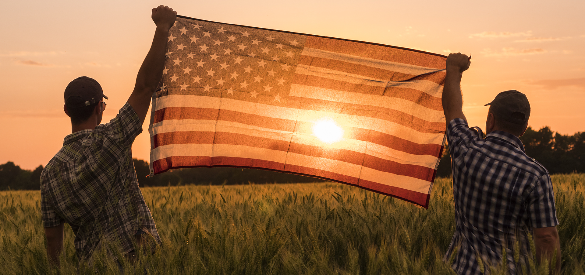 2 men holding the American Flag during sunset over a field